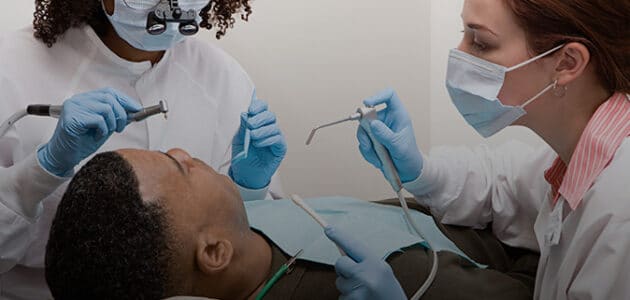 Boy leaning back in dental chair with dentists working on his mouth