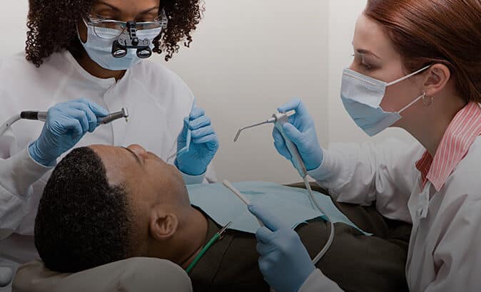 Boy leaning back in dental chair with dentists working on his mouth