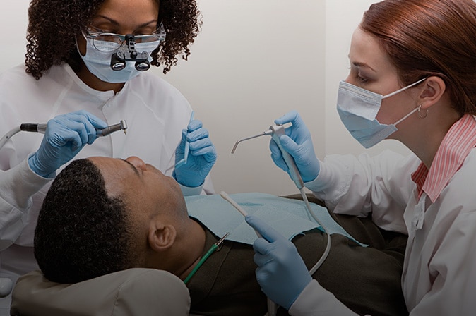 Boy leaning back in dental chair with dentists working on his mouth