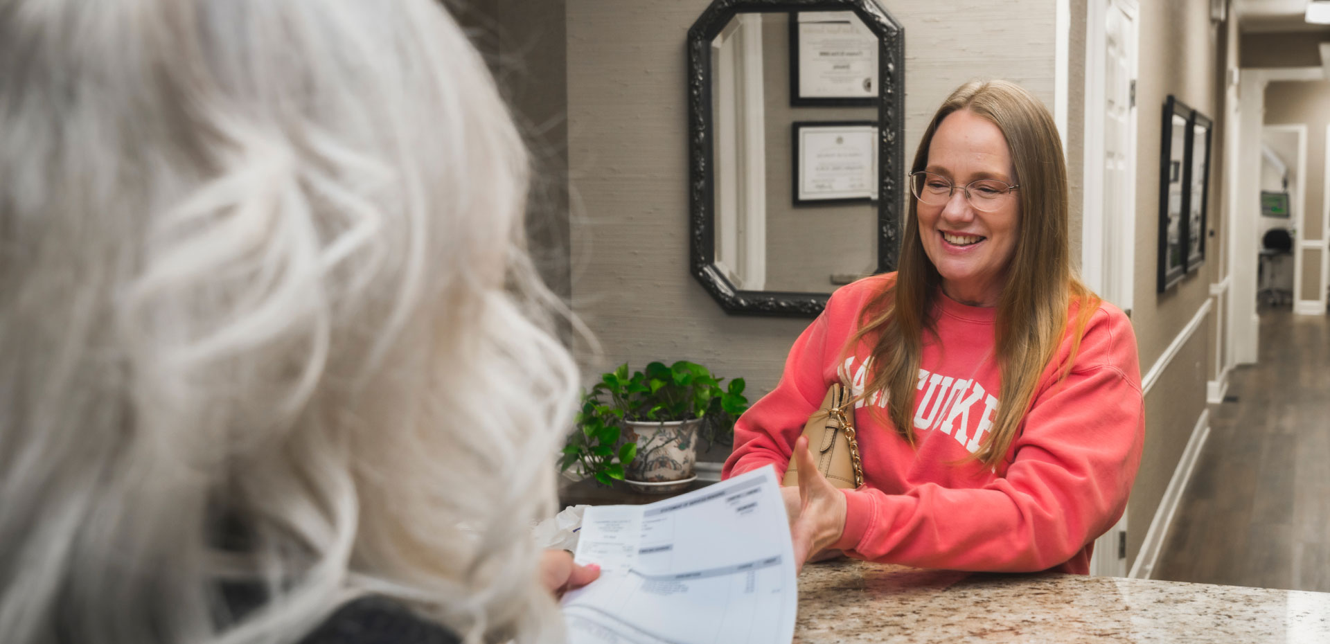smiling patient handing paperwork to team member at front desk